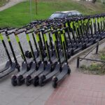 Bardzo dużo hulajnóg stojących na całej szerokości chodnika.