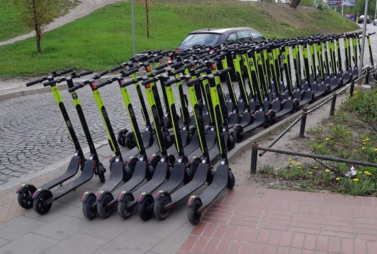 Bardzo dużo hulajnóg stojących na całej szerokości chodnika.