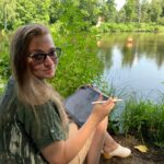 Kasia Trepkowska rysowniczka. Kobieta siedząca nad jeziorem. W ręce trzyma tablet.