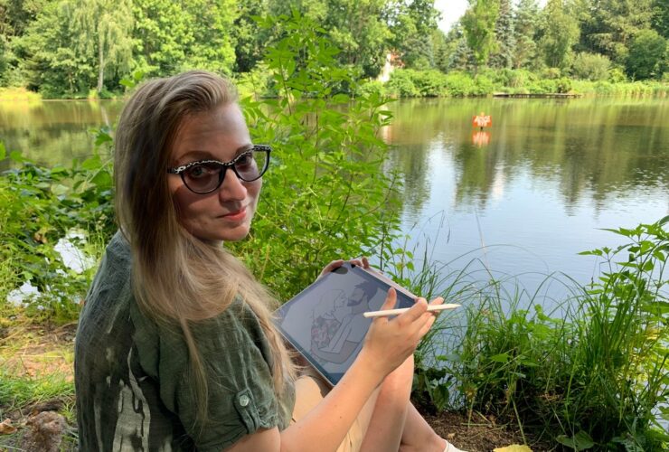 Kasia Trepkowska rysowniczka. Kobieta siedząca nad jeziorem. W ręce trzyma tablet.