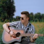 Chłopak z gitarą siedzący na trawie.