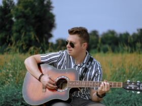 Chłopak z gitarą siedzący na trawie.