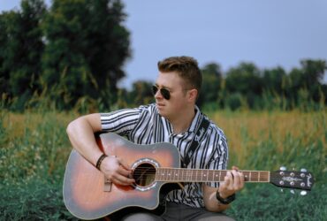 Chłopak z gitarą siedzący na trawie.