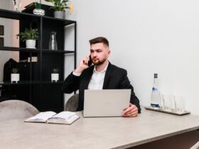 Mężczyzna siedzący przy biurku. Rozmawia przez telefon, przed nim laptop.