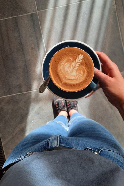 Dłoń trzymająca filiżankę z kawą. Na kawie jest wzorek serduszko.
