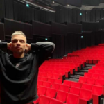 Michał Sitarski stoi w sali teatralnej. Za nim miejsca dla publiczności.