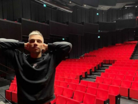 Michał Sitarski stoi w sali teatralnej. Za nim miejsca dla publiczności.