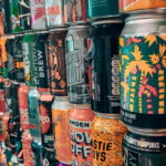 W rzędach ustawione puszki w różnych kolorach i wzorach.