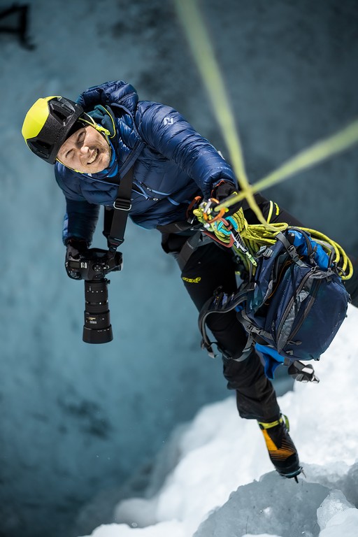 Marcin Ciepielewski wspina się po lodowcu, trzyma się liny. W ręce trzyma aparat.