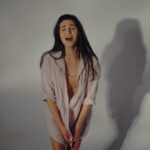 Justyna Biedrawa stoi ubrana w białą koszulę. W tle odbija się jej cień. Mimika twarzy wskazuje na to, że krzyczy.