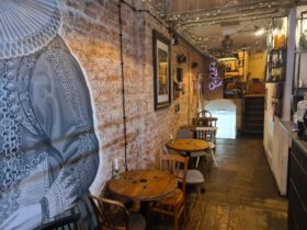 Wnętrze kawiarni w starym kadrze. Po lewej stronie stoliki z krzesłami.