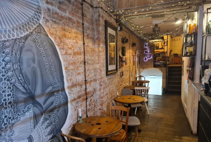 Wnętrze kawiarni w starym kadrze. Po lewej stronie stoliki z krzesłami.