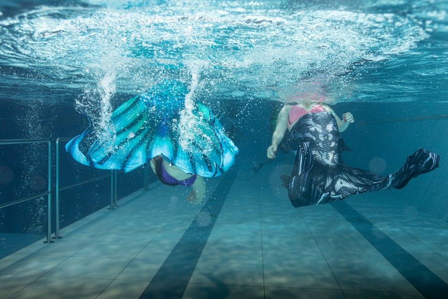 Kobiety płynące w syrenim ogonie w basenie, czyli mermaiding