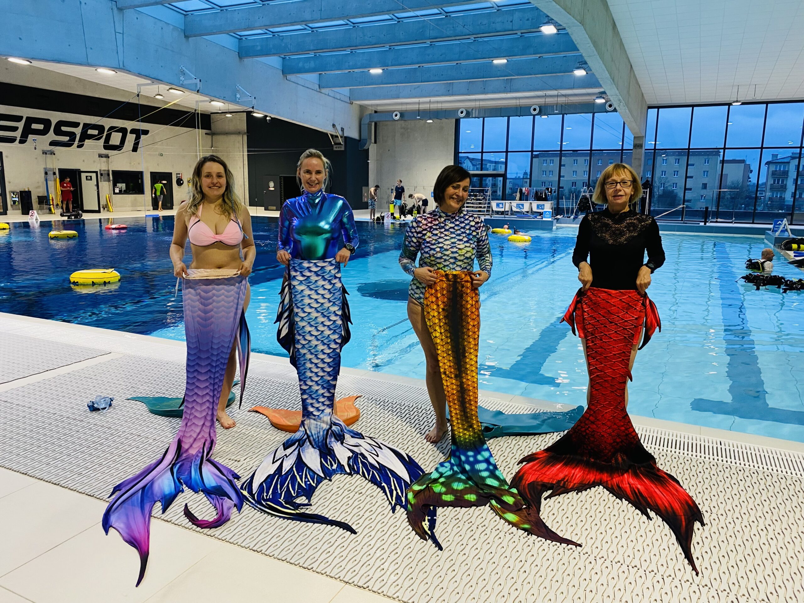 Kobiety stojące przed basenem w syrenich ogonach