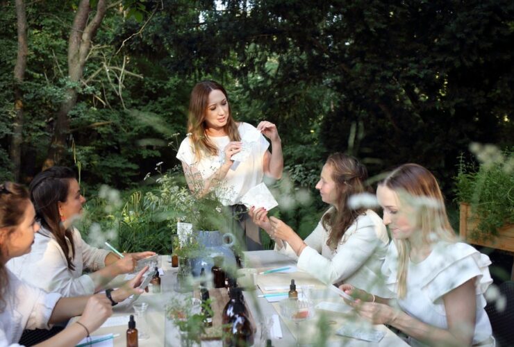 Warsztaty slou lab. Kobiety tworzą przy stole i tworzą zapachy. Agnieszka stoi przed stołem i opowiada.