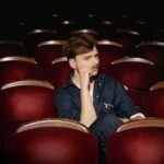 Wiktor Dyduła na planie teledysku Koło Fortuny. Siedzi na sali teatralnej.