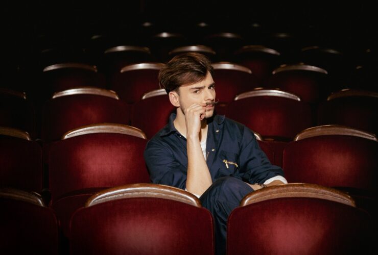 Wiktor Dyduła na planie teledysku Koło Fortuny. Siedzi na sali teatralnej.