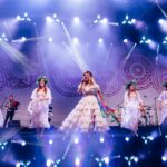 Kobiety występujące na scenie, ubrane są w długie białe suknie.